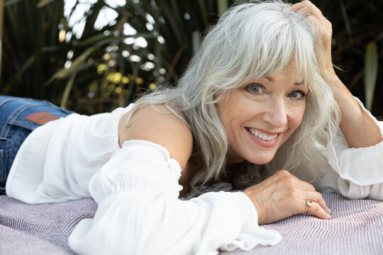 Beautiful grey haired woman in romantic blouse laying on a blanket 
