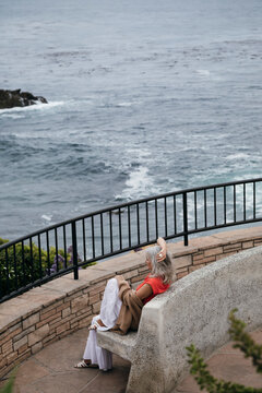Older grey haired woman sitting on bench overlooking cliffs 