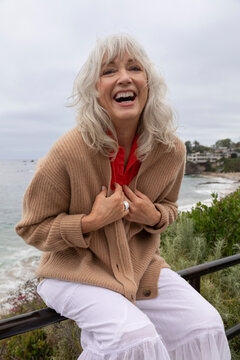 grey haired women laughing while sitting on a ledge on the coast