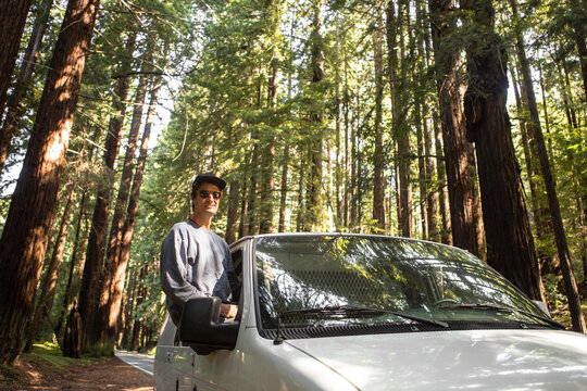 Man Sitting on Van Window Parked Among Giant Redwood Trees