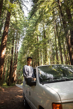 Man Sitting on Van Window Parked Among Giant Redwood Trees