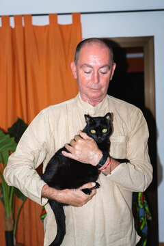 A middle-aged man with his black cat in his arms at home