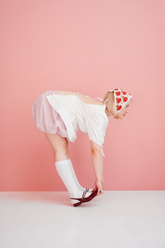 Woman bending to adjust shoe against pink background