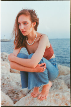 Young Woman Sitting on Rocky Shore Near sea at Sunset