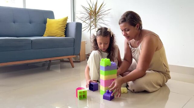 Young girl and her mother playing together, building a tall tower with colorful plastic blocks