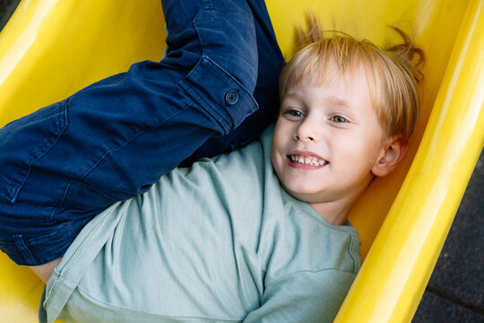 Child smiling and playing on a yellow slide at playground.