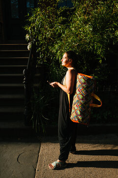 Woman standing in sunlight with yoga mat bag