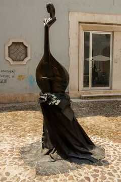 Modern statue of a woman part violoncelo in a typical stone street with historic buildings in downtown Coimbra, Portugal