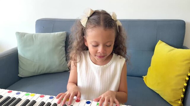 Cute little girl with curly hair practicing on a digital piano keyboard in her living room