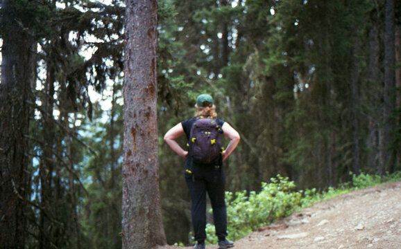 Woman standing alone on the side of a forest trail, Alberta, Canada