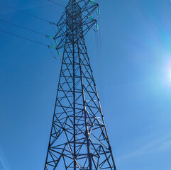 Torre de alta tensi&oacute;n de estructura met&aacute;lica bajo un cielo azul despejado con el resplandor del sol