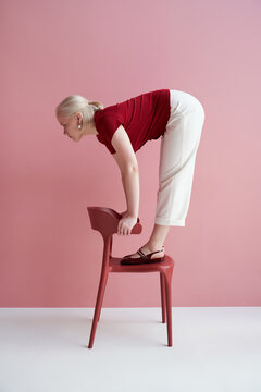 Woman balancing on chair against pink wall