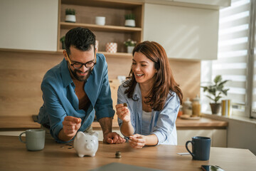Happy couple saving money in piggy bank at home kitchen