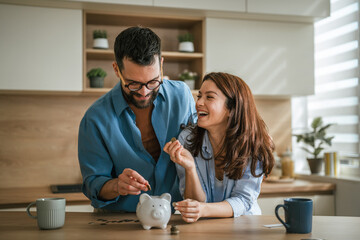 Happy couple saving money in piggy bank at home kitchen © Miljan Živković