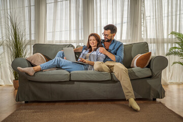 Couple using laptop together on sofa at home
