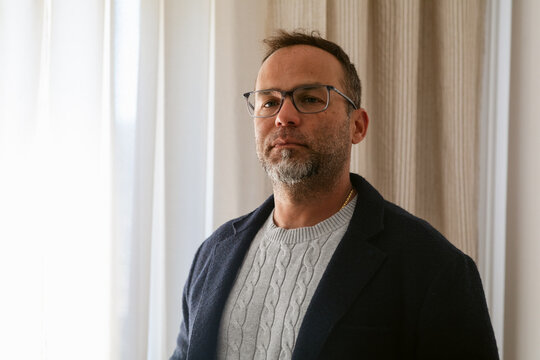 Man in a Sweater Poses Indoors Near Large Windows