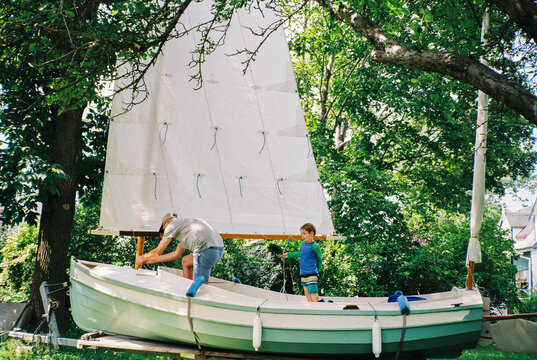 Father and son work on sailboat in yard