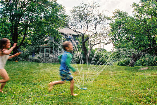 Motion blur kds playing in backyard sprinkler