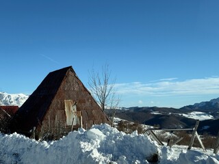 Rustic triangular barn in snow with mountain landscape under clear blue winter sky
