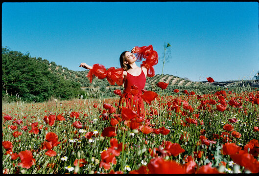 Young woman in a poppy field with arm raised