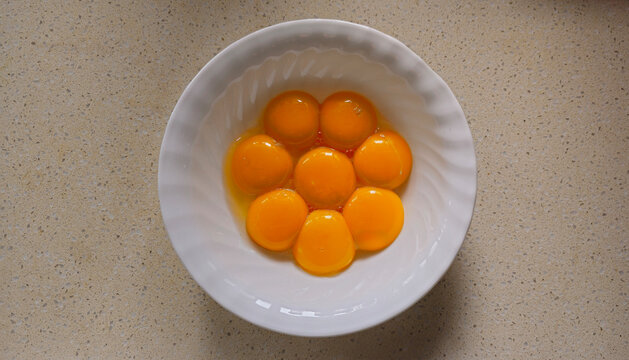Five cracked raw eggs in a white mixing bowl ready for baking, cooking preparation, and recipe setup
