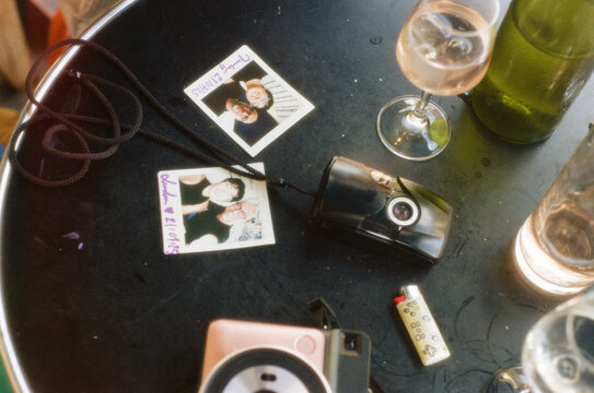 Polaroids prints, film and instant camera, and wine on a cafe table