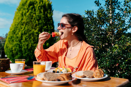 Young woman eating delicious fruit for breakfast outdoors