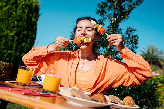 Young woman eating delicious fruit for breakfast outdoors