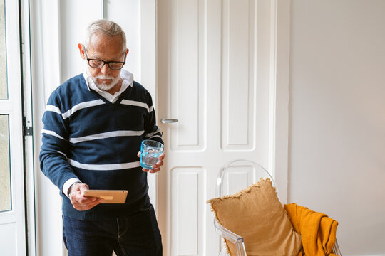 Grey-haired senior man with beard and eyeglasses standing indoors hold