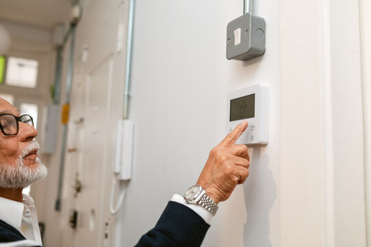 Senior Adjusting Thermostat in Modern Home During Day