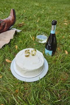 Women's brown cowboy boots, champagne and cake on grass