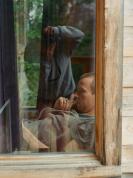 Man reading behind a window of a cabin.