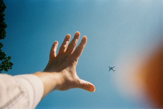 Hand reaches towards airplane in sky