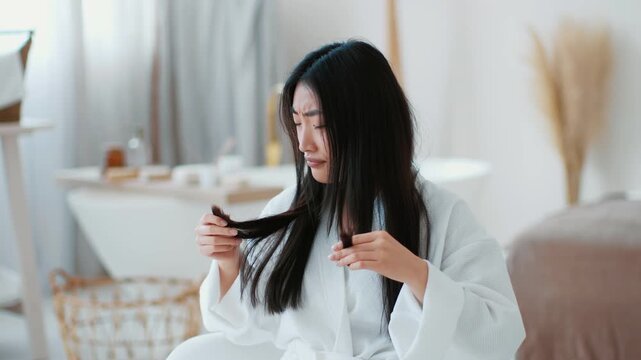Hair Care problems. Young upset asian woman looking at her split ends and frowning face, feeling displeased of her hairstyle condition, slow motion, free space