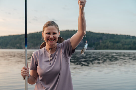 Smiling Woman Holding a Freshly Caught Fish at Lakeside