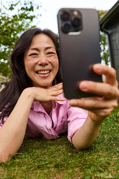 Middle aged asian woman taking selfies on grass outside