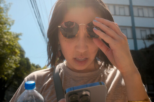 Young Person Checking Phone While Holding a Water Bottle Outside