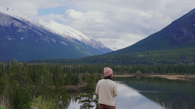 Woman standing by Vermilion Lakes looking at Mount Rundle reflecting in water in Banff National Park