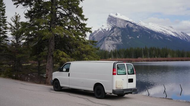 White camper van parked beside Vermillion Lakes with mountains and forest in Banff National Park