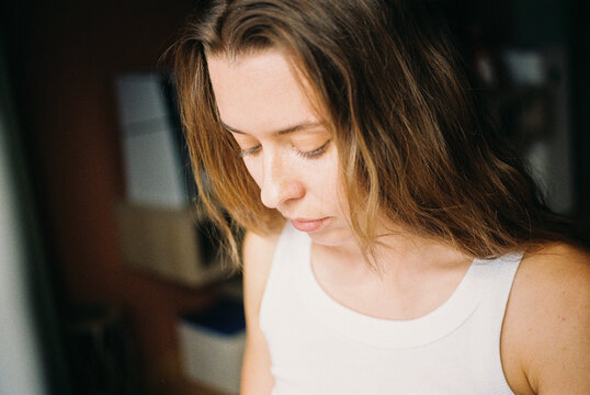 Woman in white tank top looking down in soft natural light