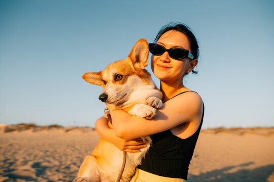 Woman Enjoys Sunset at the Beach While Holding Her Corgi