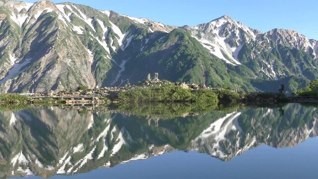 朝日を浴びた新緑の八方池と登山者
