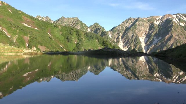 朝日を浴びた新緑の八方池と登山者
