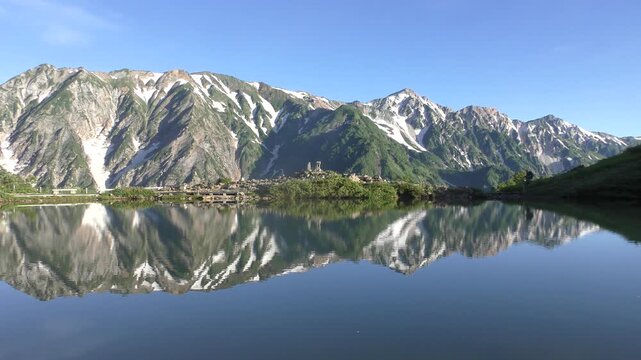 朝日を浴びた新緑の八方池と登山者
