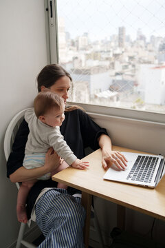 Mother Working on Laptop While Caring for Baby in Modern Apartment