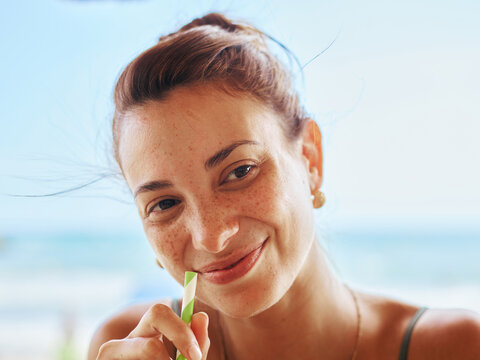Smiling Woman Enjoying a Refreshing Drink by the Beachside
