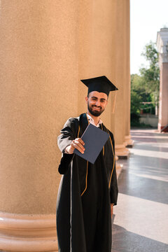 Asian man wearing graduated uniform holding diploma at university.