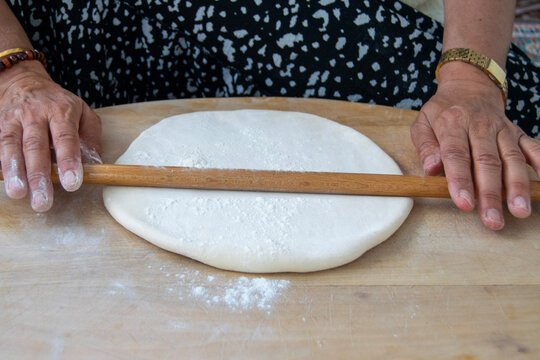 Hands Rolling Dough on Wooden Surface with Rolling Pin