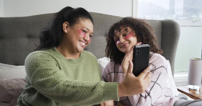 African American mother and daughter holding phone, posing, reviewing, adjusting gel patches on bed
