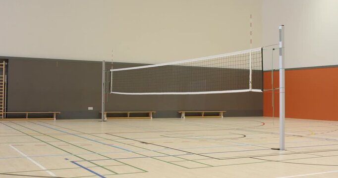 Volleyball net sagging progressively after tension release off-camera between posts in gymnasium